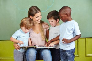 Happy child day care worker with children reading a book in kind